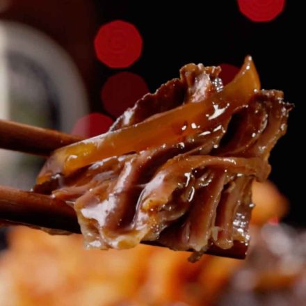 Tender braised beef short ribs being lifted with chopsticks, showing glossy Korean-inspired sauce coating the meat