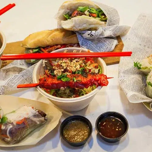 Vietnamese steak vermicelli bowl with grilled meat, noodles, vegetables, and dipping sauces, plus wrapped spring rolls