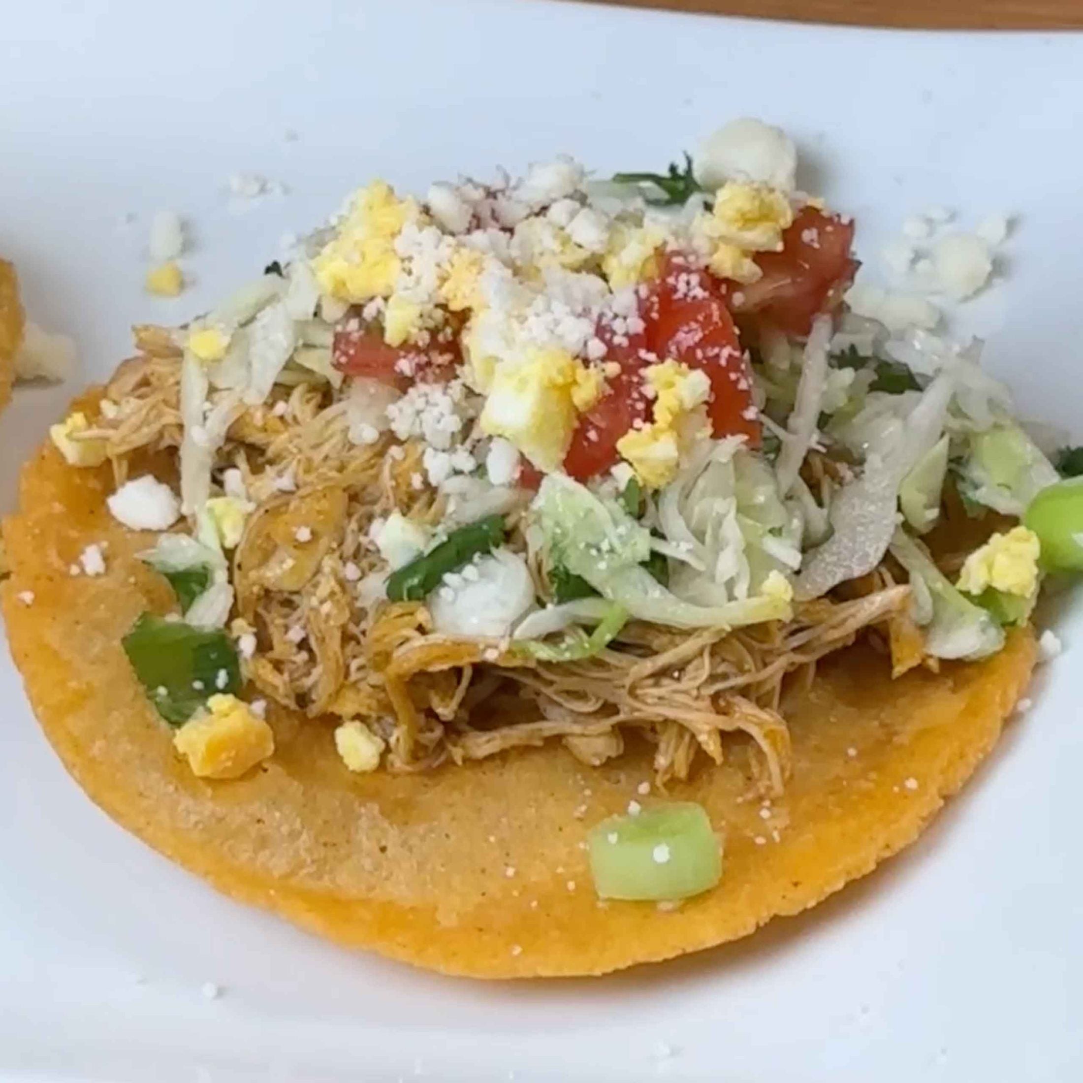 Crispy corn tortilla topped with shredded meat, lettuce, tomatoes, cheese, and hard-boiled egg - traditional Belizean salbute