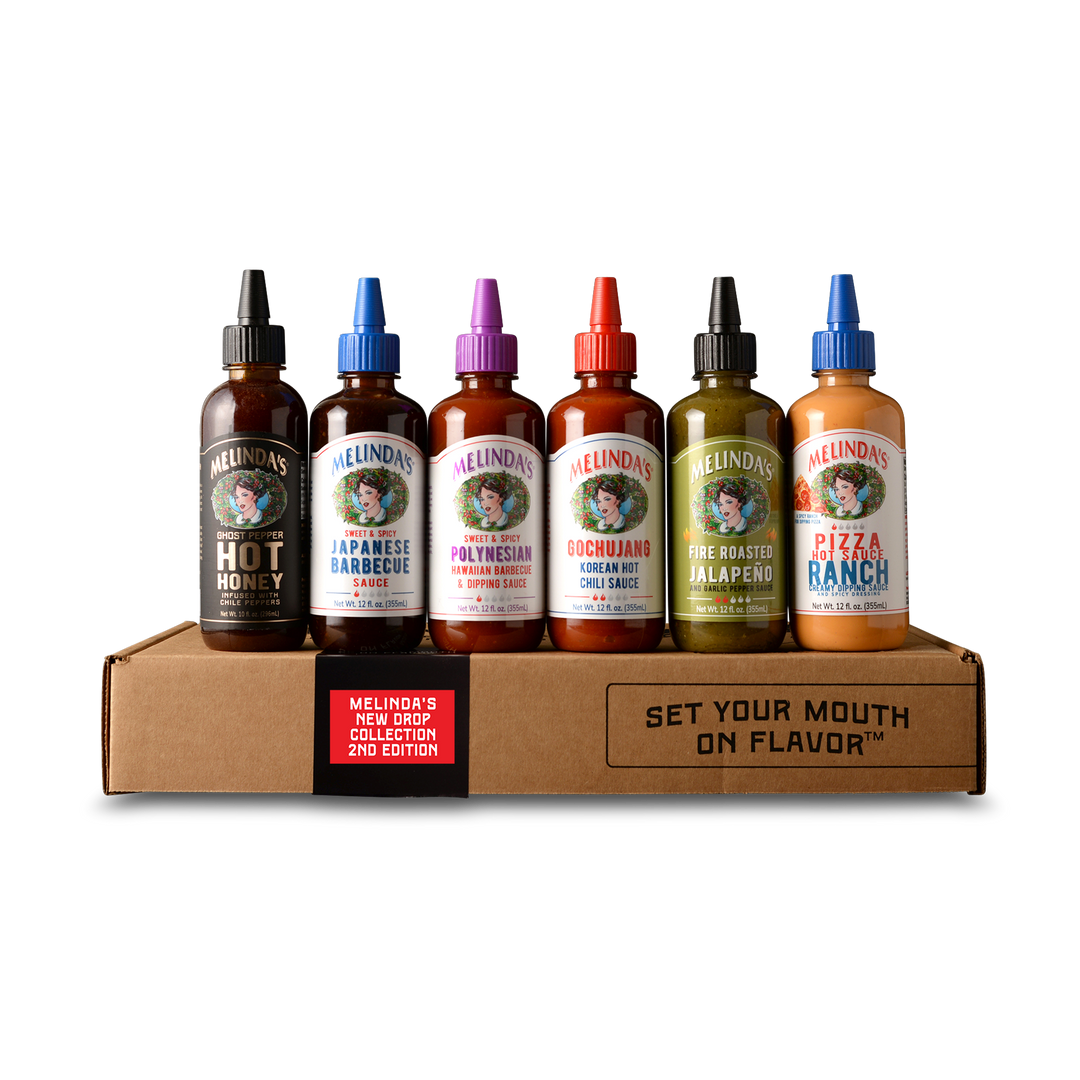 Six Melinda's hot sauce bottles with colorful caps arranged on a cardboard box labeled "SET YOUR MOUTH ON FLAVOR"