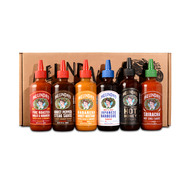 Six Melinda's hot sauce bottles with colorful caps displayed in front of cardboard box featuring various flavors
