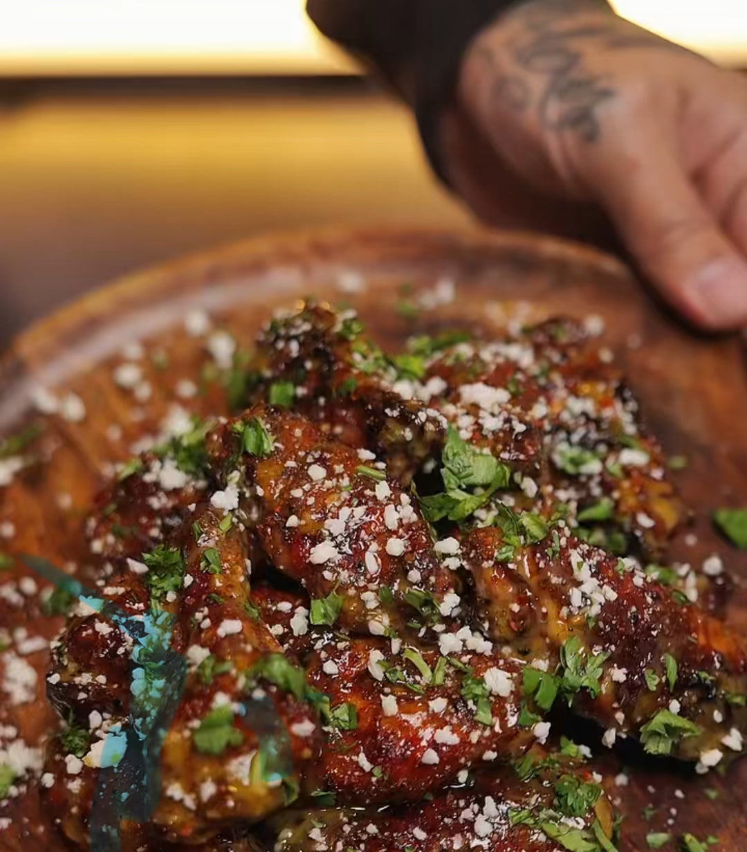 Glazed chicken wings garnished with fresh herbs and crumbled white cheese in a rustic clay bowl