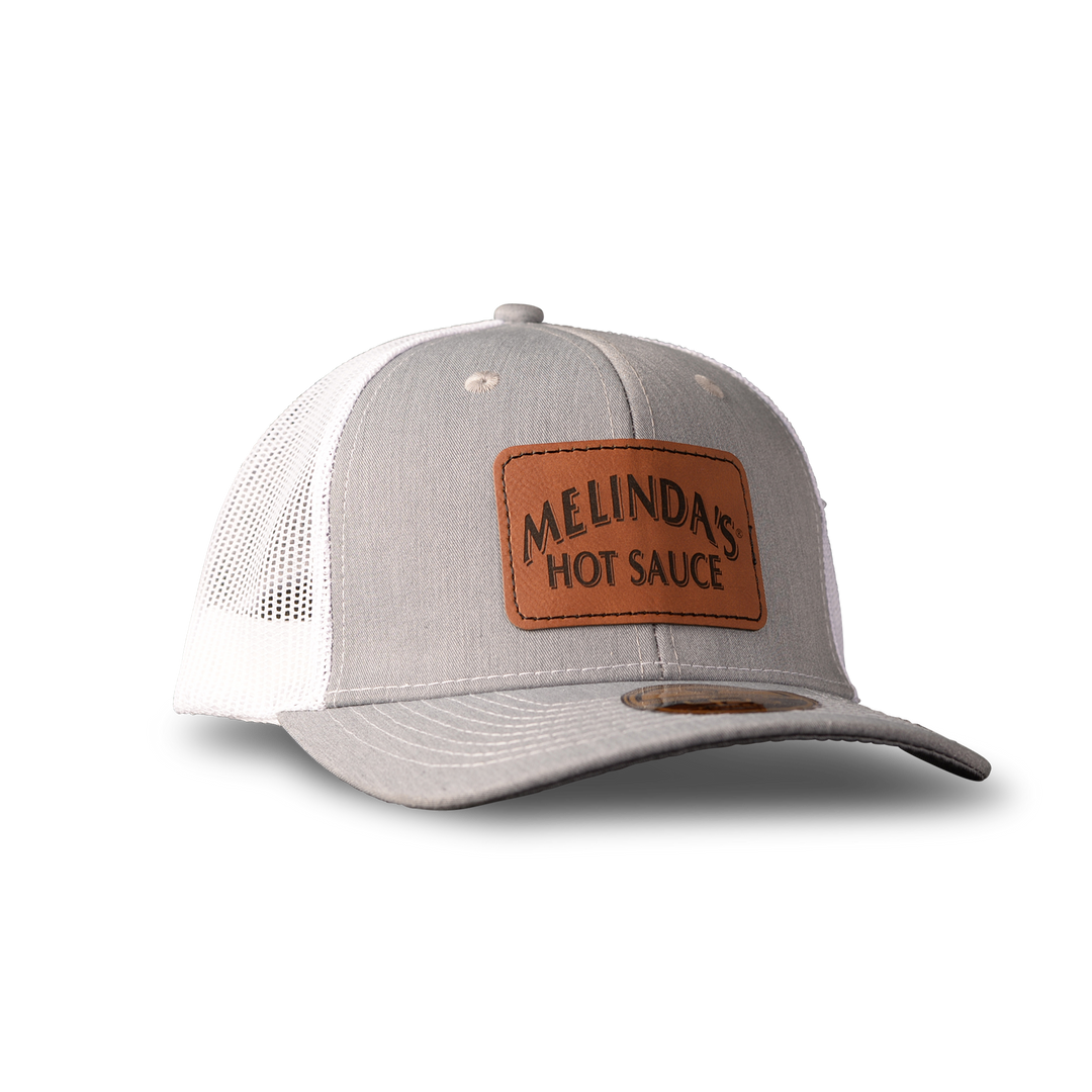 Gray and white trucker hat with brown leather patch reading "Melinda's Hot Sauce" on front panel