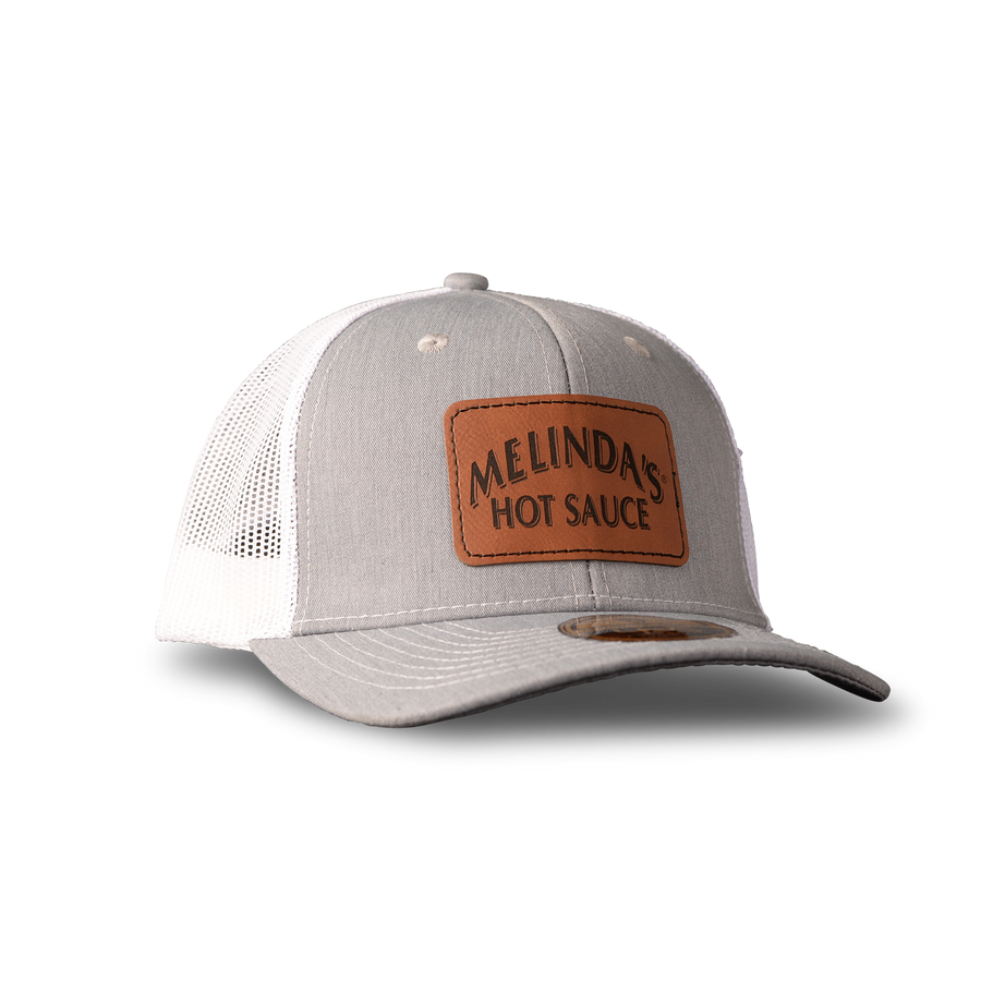 Gray and white trucker hat with brown leather patch reading "Melinda's Hot Sauce" on front panel