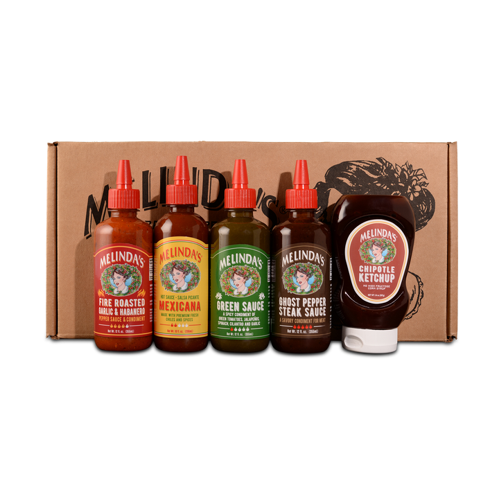 Five Melinda's hot sauce bottles with red caps and one chipotle ketchup bottle displayed in front of brown cardboard box