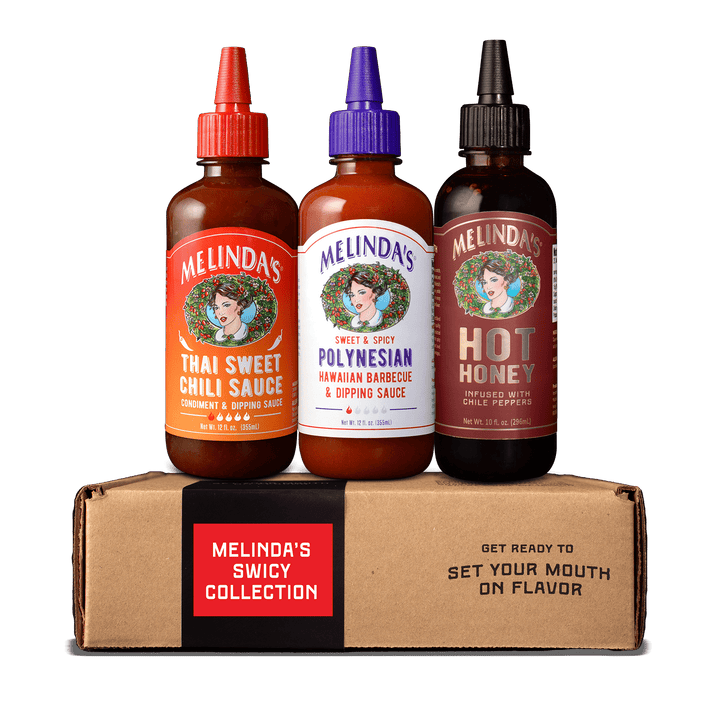 Three Melinda's sauce bottles with colorful caps on cardboard box labeled "Melinda's Spicy Collection"