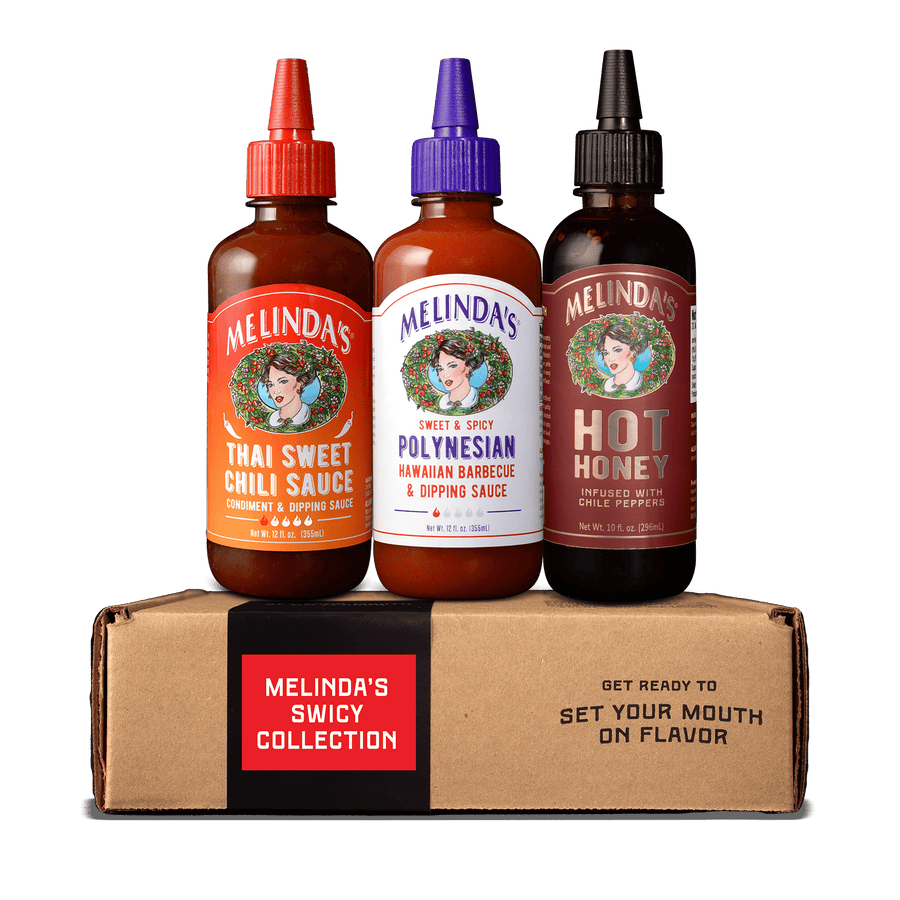 Three Melinda's sauce bottles with colorful caps on cardboard box labeled "Melinda's Spicy Collection"