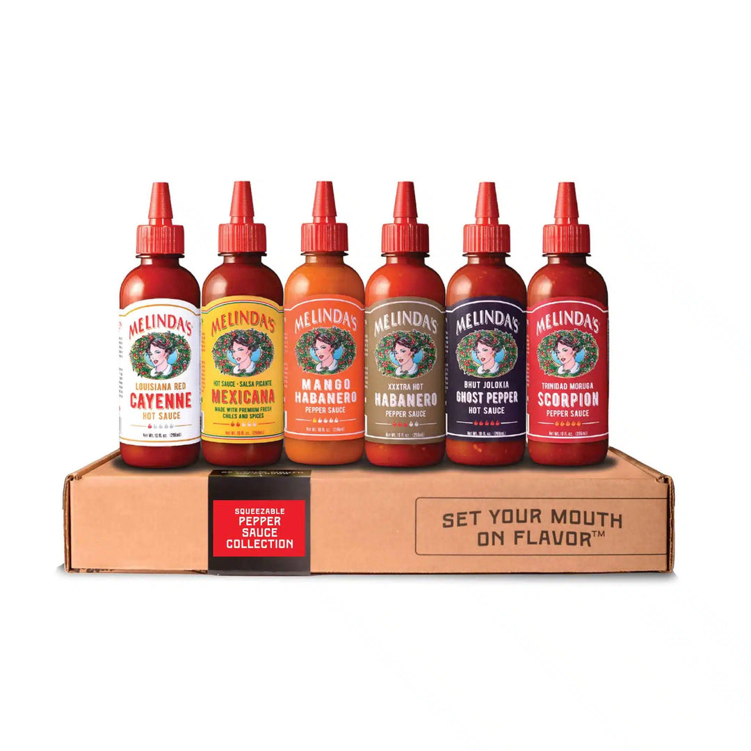 Six Melinda's hot sauce bottles in different flavors displayed on cardboard box with "Set Your Mouth on Flavor" text