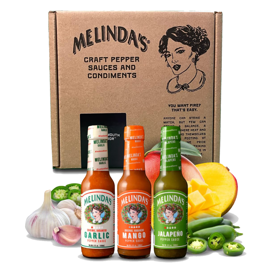 Melinda's hot sauce gift box with three bottles - garlic, mango, and jalapeño flavors - alongside fresh peppers and...