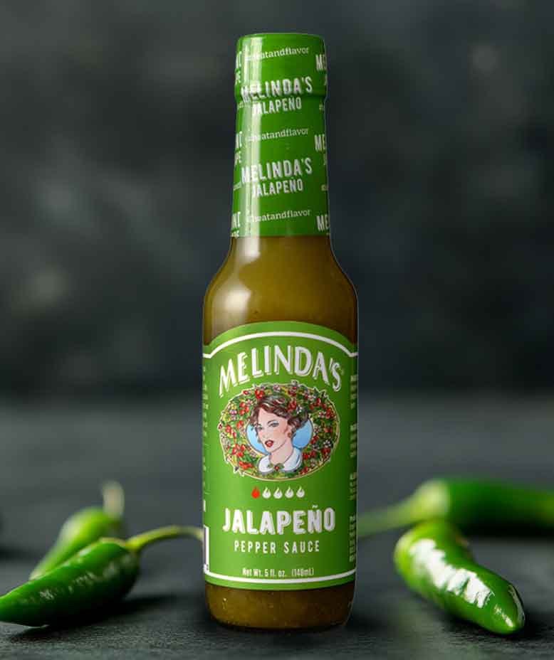 Melinda's Jalapeño Pepper Sauce bottle with green label and fresh jalapeño peppers on dark background